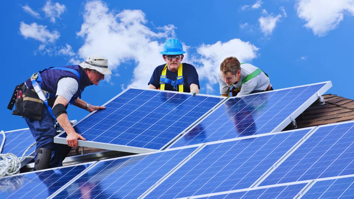 Drie installateurs tillen samen een zonnepaneel op het dak